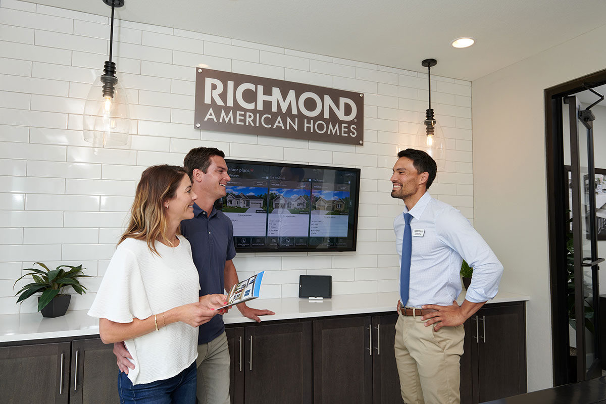 Real estate agent presenting bright, empty room with sliding doors to smiling couple