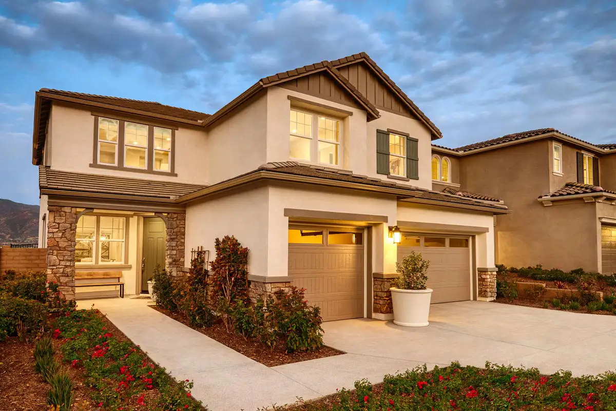 Two-story home with lights on, with three-car garage and sidewalk to small front porch and front door