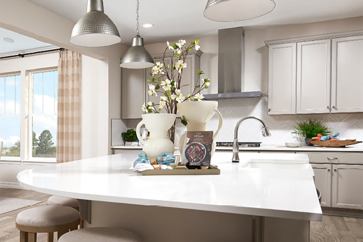 Kitchen with large island rounded on two sides, herringbone backsplash, and three hanging lights