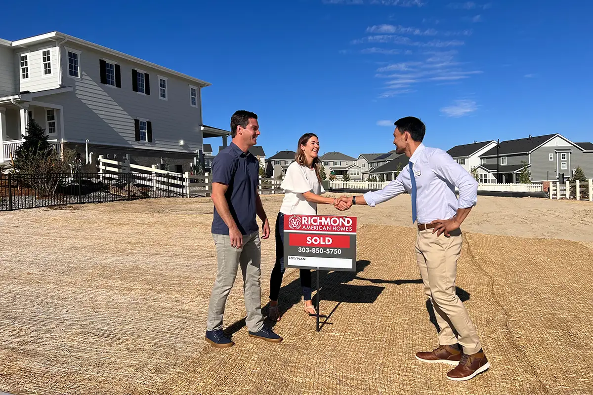 Couple shaking hands with Richmond American Homes sales associate behind 'sold' sign on empty lot