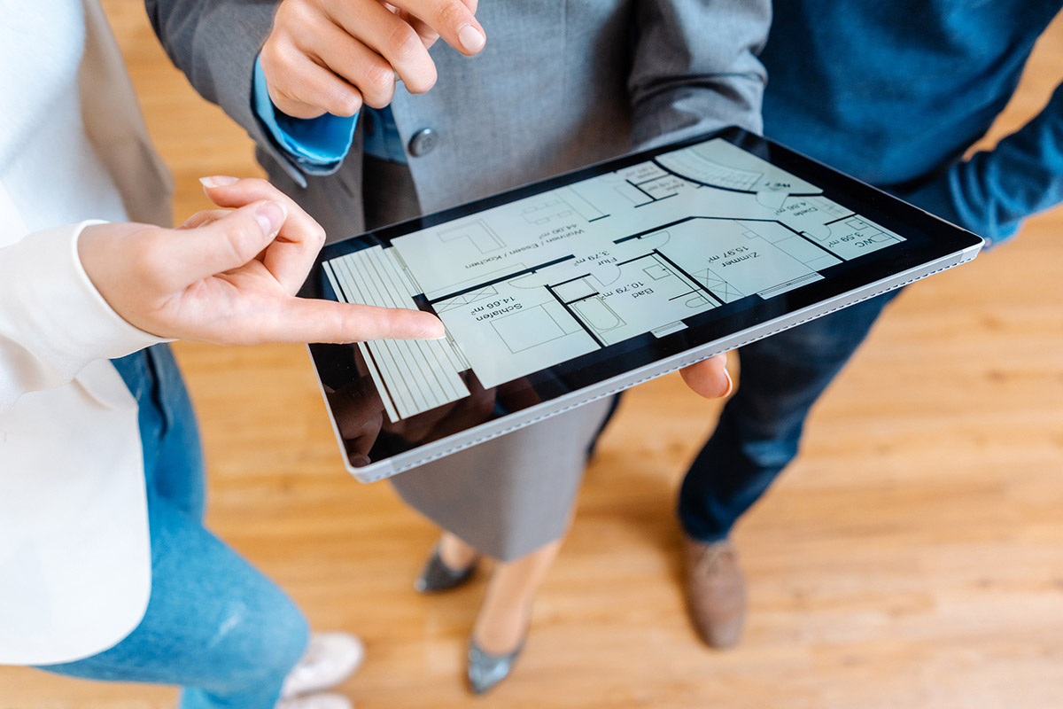 Someone holding tablet showing blueprints to two other people