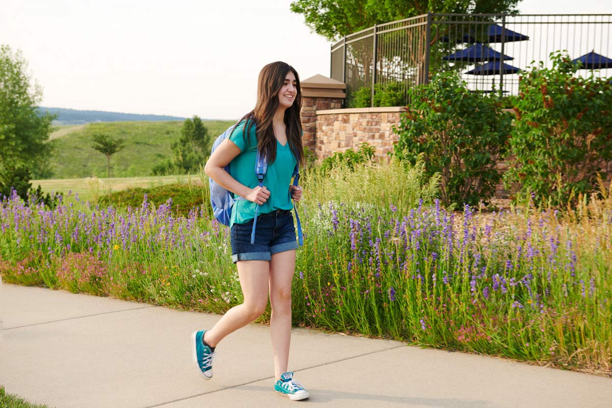 Teenage girl walking on sidewalk with backpack on