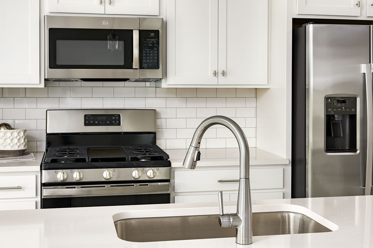 Detail of sink, white cabinets and microwave with subway-style backsplash