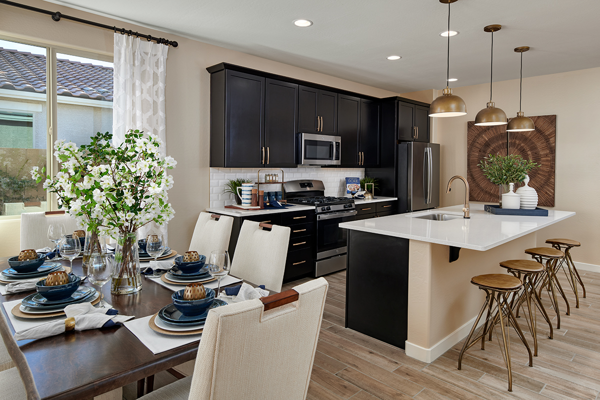 Dining table next to kitchen with black cabinets and gold hardware and island with four chairs