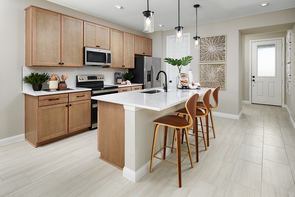 Kitchen with light wood cabinets and white countertops and an island with three barstools