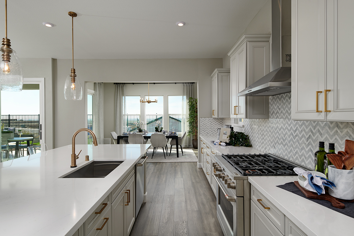 Large kitchen with large island, gold hardware, and chevron backsplash, with dining room in the background