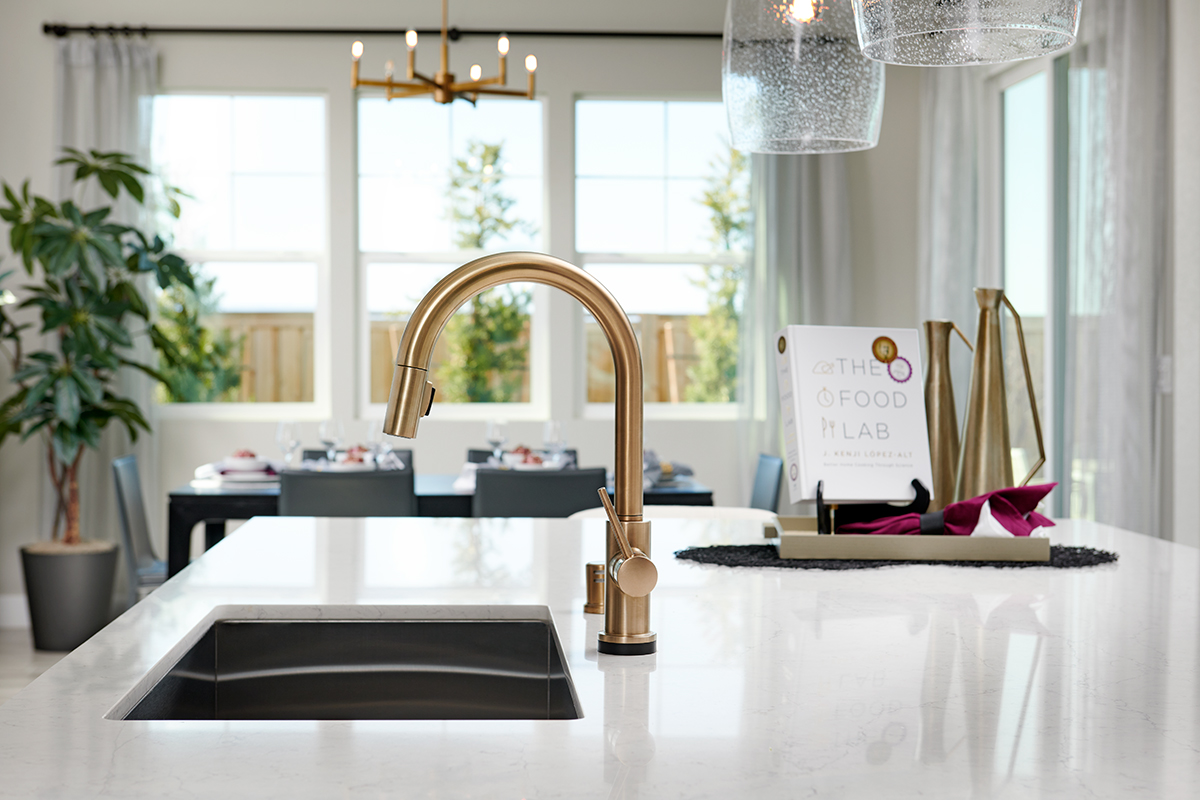 Island with quartz countertop, double sink, and gold faucet in front of dining area with three windows