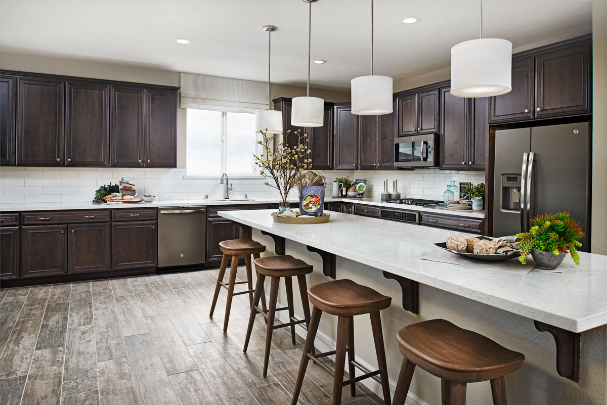 Large kitchen with dark cabinets and a long island with four light fixtures above it