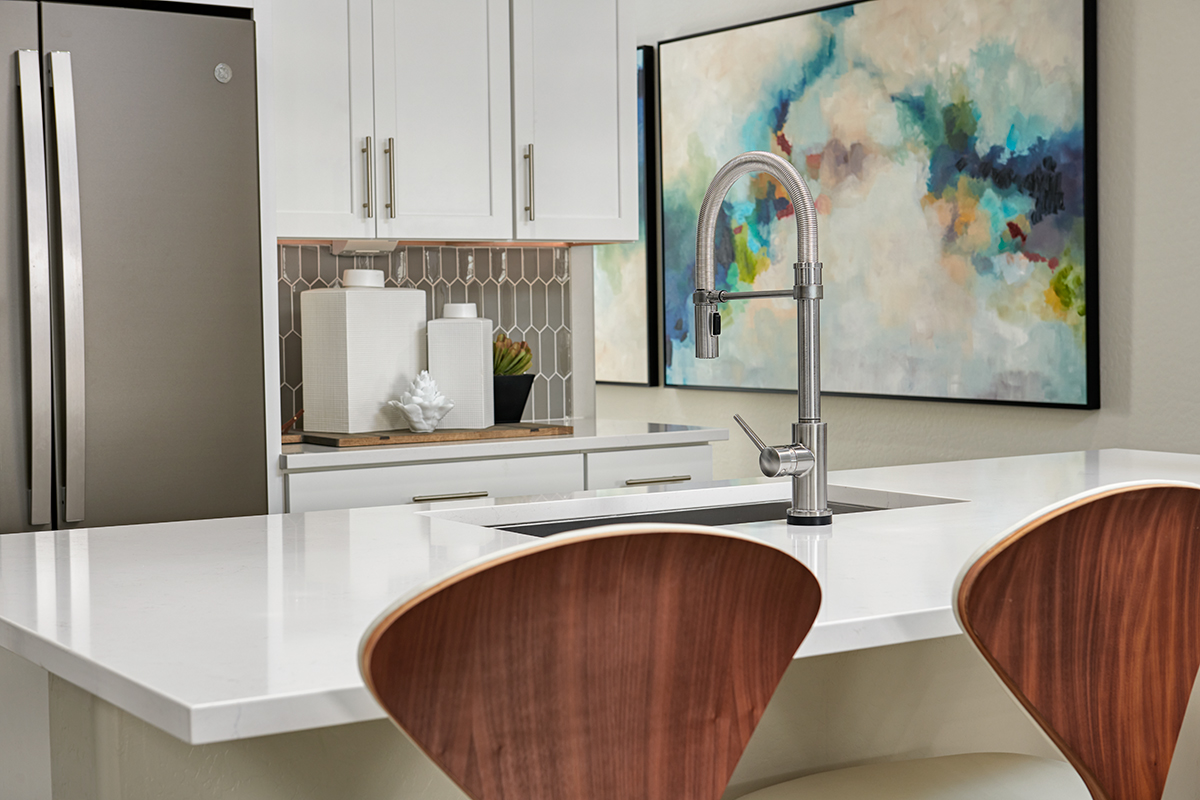 Kitchen island with tall faucet in front of refrigerator and cabinets with picket backsplash