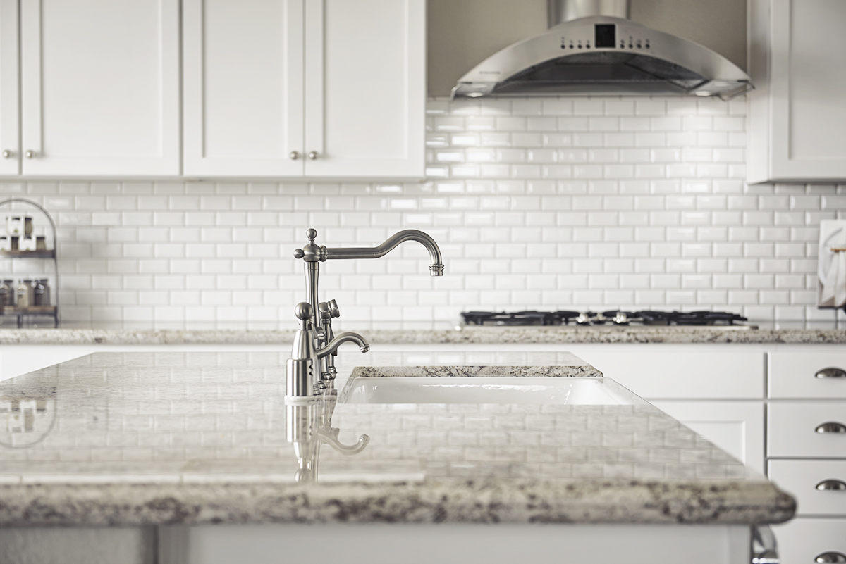 Island with granite countertop in front of cabinets with brick-style backsplash