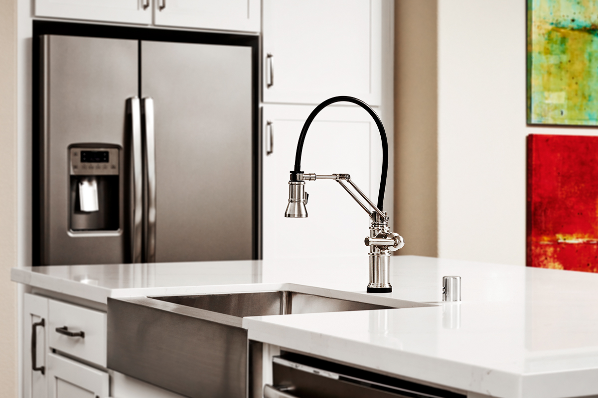 Silver farmhouse kitchen sink on island with modern faucet and refrigerator in the background