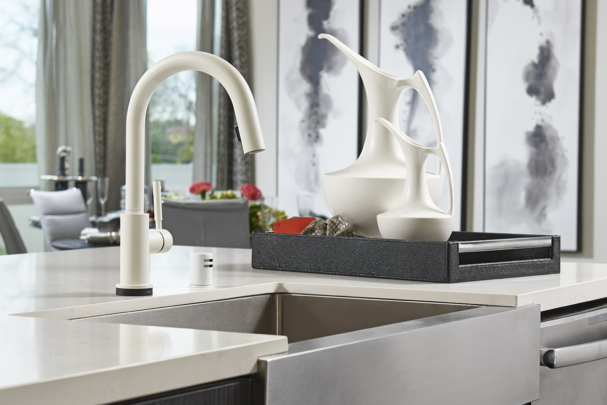 Silver farmhouse kitchen sink on island with white facuet and dining room in background