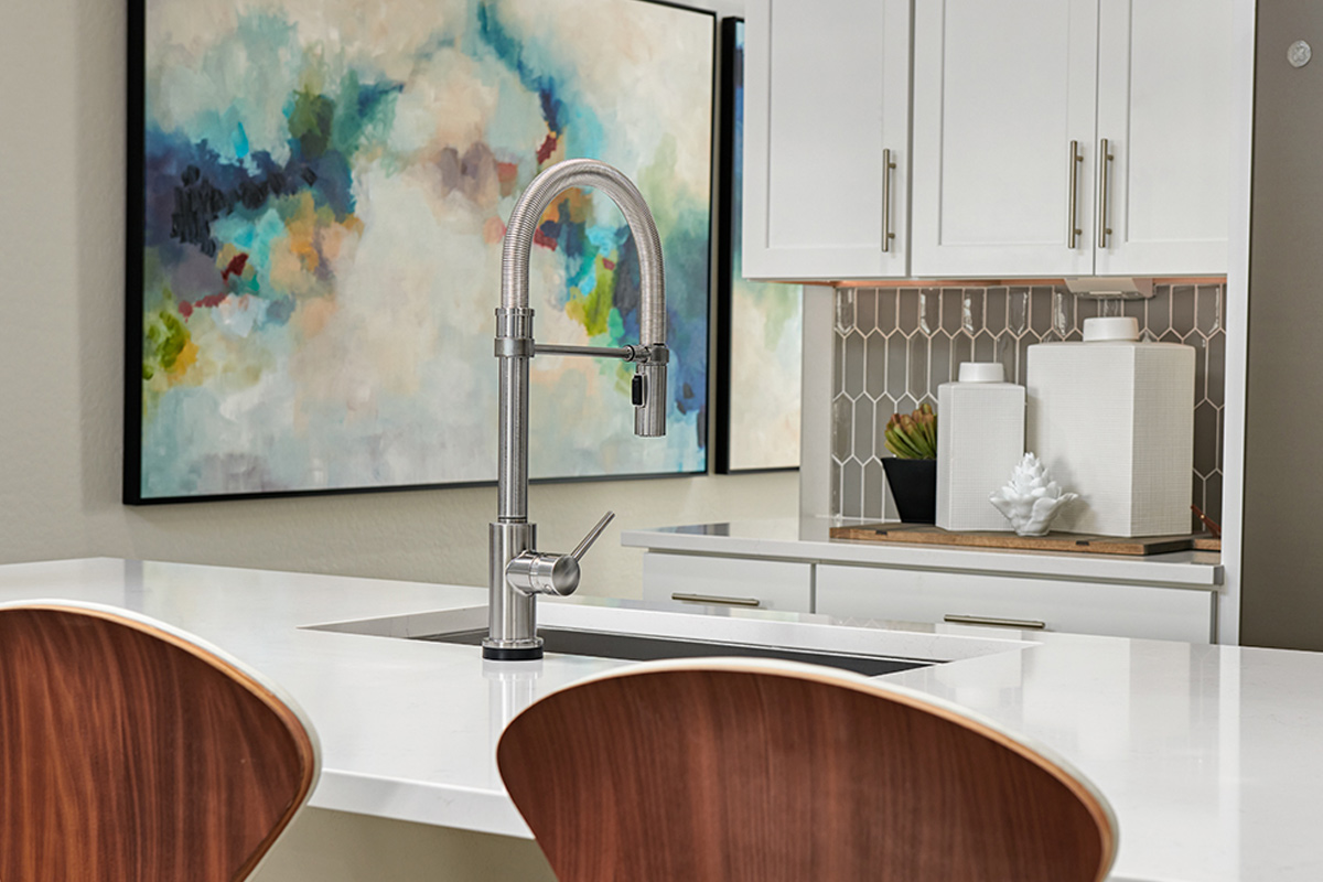 Two chairs in front of island with large sink and faucet, with cabinets and picket backsplash behind it