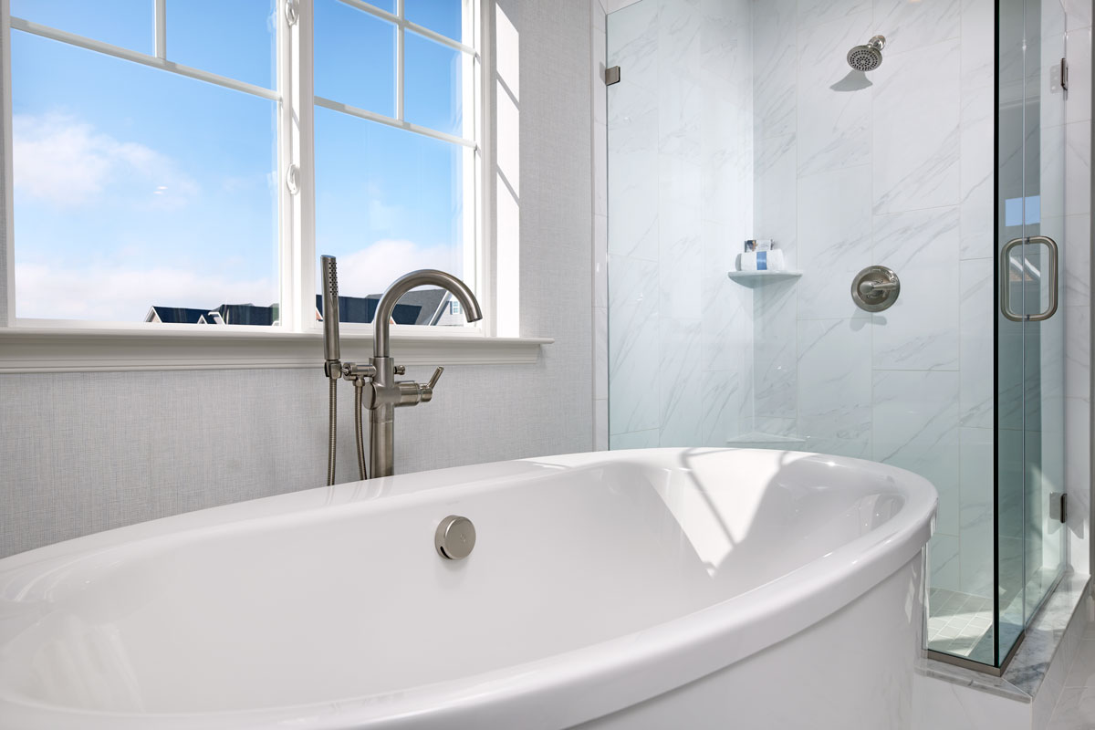 Tub with tall silver faucet in front of shower stall with silver showerhead